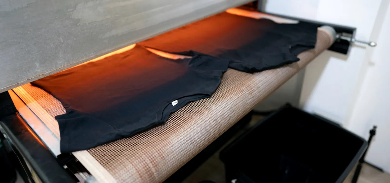 เสื้อสีดำกำลังออกจากช่องอบของ Conveyor Dryer